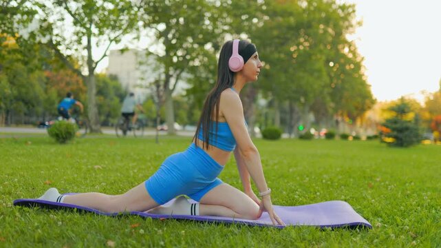 Fit female model stretching on a purple yoga mat in the sunny summer park.