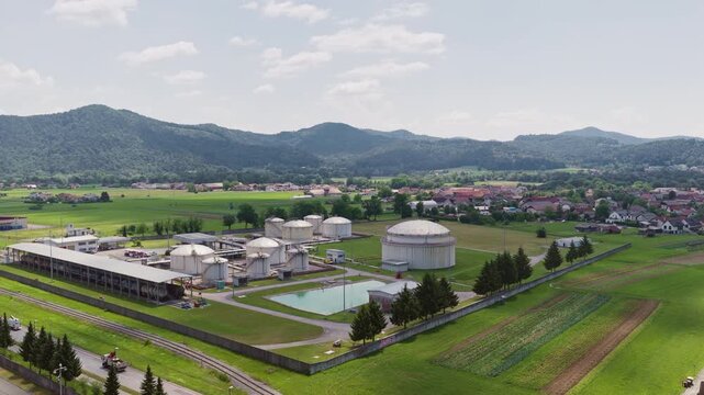 Large industrial oil storage tanks are seen at a petroleum depot with green fields nearby. The view shows energy infrastructure in the area.
