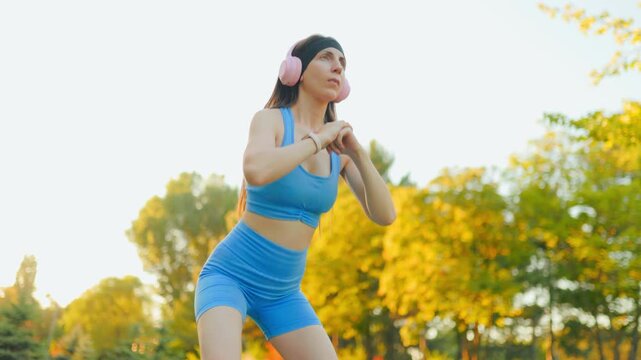 Athletic female doing intense squat exercise in the sunny autumn park outdoors.