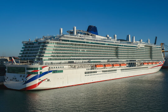 Massive gigantic modern cruiseship cruise ship liner Iona or Arvia in Cadiz, Spain during summer Mediterranean cruising with harbor and container port infrastructure