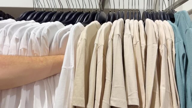 Assorted Casual Clothes on Store Racks.Hand Choosing Clothes on Hangers in Clothing Boutique &ndash; Casual Wear Selection