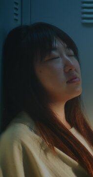 Young Woman Leaning against Lockers, Lost in Thought While Coping with Pressure and Emotional Fatigue. Concept of Mental Health, Stress, Burnout, Resilience and Everyday Challenges. Vertical Shot.
