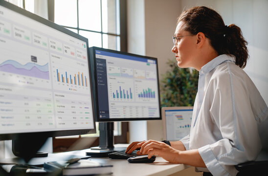 Businesswoman Analyzing Data on Multiple Monitors in Modern Office