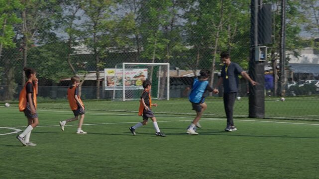 Youth Soccer Player Dribbling Ball Across Outdoor Field During Energetic Practice Match with Teammates and Goalkeeper, Training on Artificial Turf with Coach in Green Park Setting