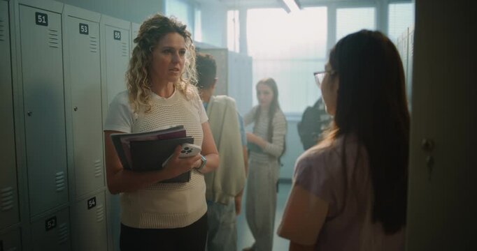 Friendly Female Teacher Speaks with Teenage Student beside School Lockers before Class. Warm Educational Moment, Mentorship, Academic Support, Positive Communication in Modern School Environment.