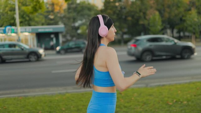 Side profile of a fit young woman jogging outdoors in the sunny city park.
