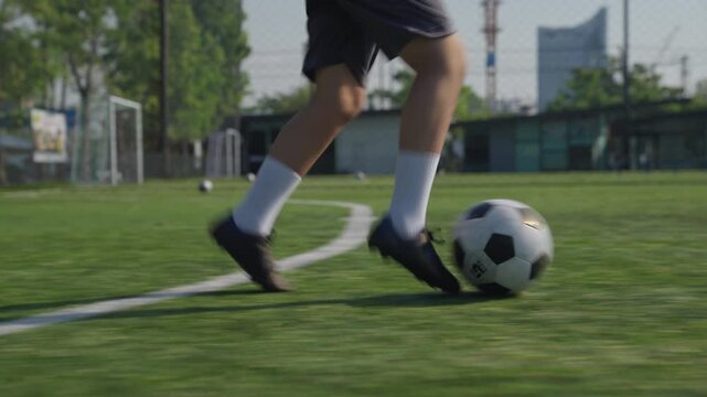 Soccer Player Dribbling Ball Across Artificial Turf During Outdoor Practice, Motion Blur, Athletic Movement, Concentration, Urban Background, Fenced Sports Field Training