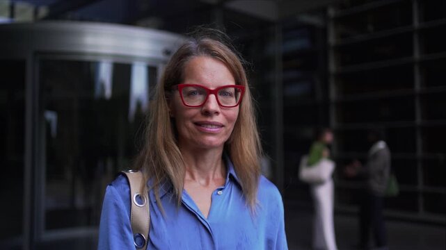 Portrait of a mature professional woman looking at the camera cheerfully, in front of a modern business center.