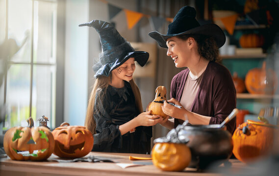 Happy Mother and Daughter in Witch Costumes Carving Pumpkins for Halloween