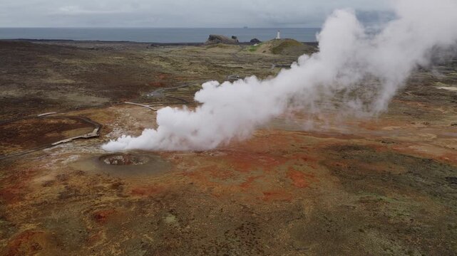 Gunnuhver Geothermal Area, Reykjanesbaer, Southern Peninsula, Iceland, revealing a powerful steam plume, hydrothermal deposits, altered volcanic ground and Reykjanesviti Lighthouse, drone pullback.