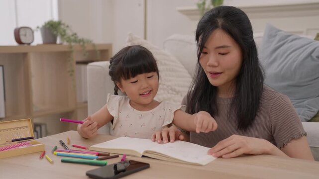 Asian mother and woman parent helping daughter child with homework, drawing, reading, writing, education and creative learning at home, sharing warm family moments together in cozy room