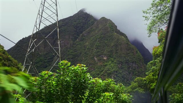 Train Machu Picchu Peru Rail Sacred Valley jungle Ollantaytambo in route Aguas Clientes Urubamba river Peru Peruvian Andes mountains range peaks Inca Trail rainy season cloudy tower pan up