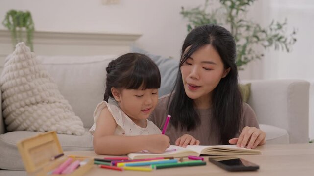 Mother and Daughter Child Family Drawing with Pencil Education at Home, Sharing Warm Creative Learning Moment at Table with Notebook, Open Book, Colorful Art Supplies and Joyful Activity