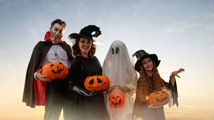 Fototapeta premium Happy Family in Halloween Costumes with Pumpkins at Sunset