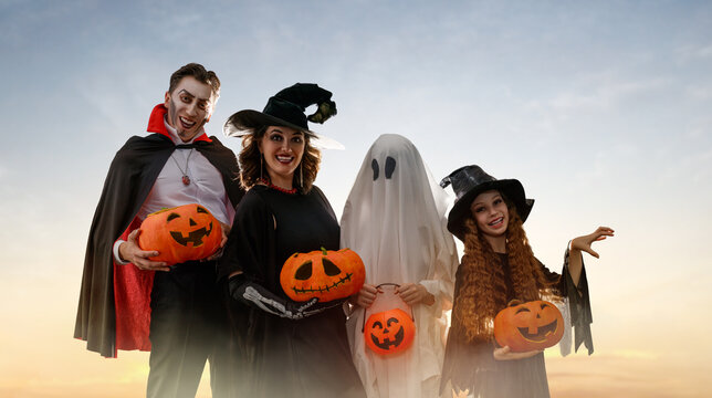 Happy Family in Halloween Costumes with Pumpkins at Sunset