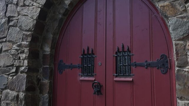 Detailed shot of a weathered red arched church door in Olinda Melbourne, framed by rustic stonework. Moody natural lighting highlights ornate black ironwork and vintage gothic design.