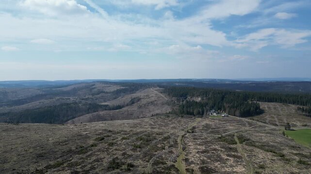 Drone view of the rugged Thuringian landscape in Germany. This remote, peaceful scene features deforested hills, evergreen forests, and a solitary building under a cloudy sky.