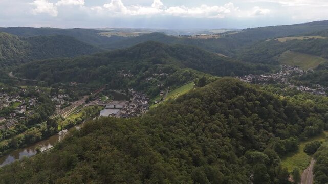 Aerial push in shot of Obernhof village nestled in the lush Lahn valley, Germany. Features the winding Lahn river, a bridge, and surrounding hills like Himmelsberg and Bernshahner Kopf.