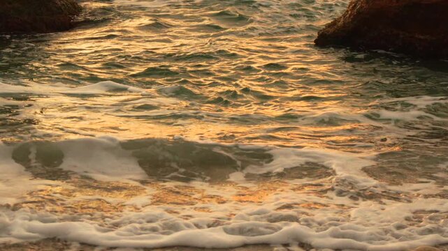 Waves, ocean, golden hour light reflecting beautifully on turquoise seafoam water washing onto a rocky beach at sunset.