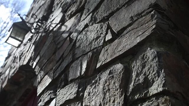 Cinematic close-up shot pans textured stone wall and wrought-iron lantern of an old Olinda Melbourne church. Dramatic angled sunlight highlights rustic masonry and antique architectural details.