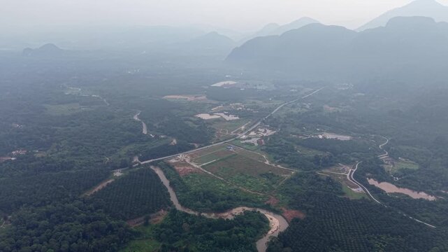 Drone aerial of misty valley with winding river, fields, forests and distant layered mountain silhouettes at Kampar, Perak