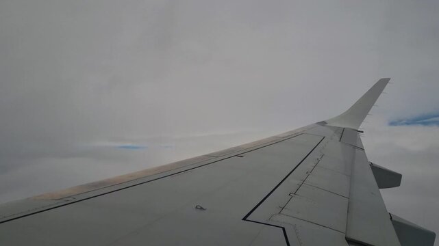 View from an aircraft window as the wing passes through dense overcast clouds, creating a moody aerial scene that evokes in-flight turbulence, air travel and commercial aviation