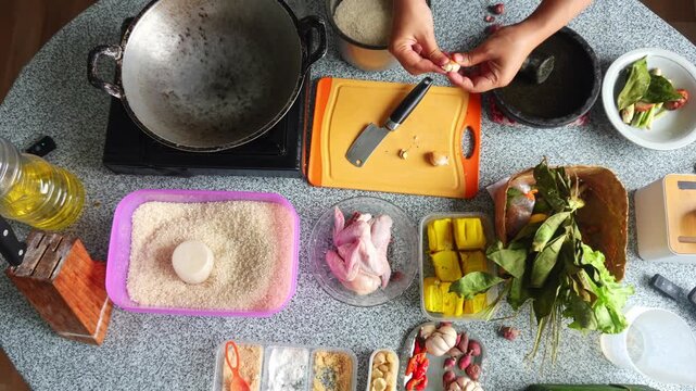 Overhead view of chef peeling and slicing garlic cloves on orange board during kitchen preparation