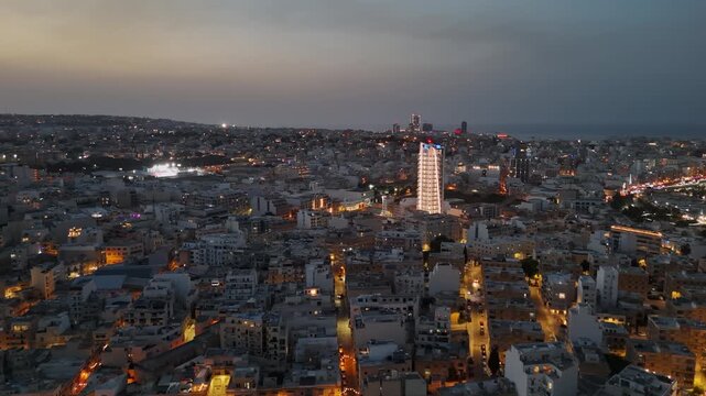 Ta' Xbiex, Malta cityscape with marina and waterfront along Gzira at dusk, illuminated streets, traffic and modern buildings in a panoramic aerial night overview.
