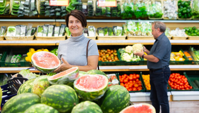 elderly woman chooses watermelon in fruit and vegetable section