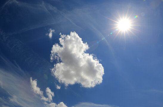 Bright sun shines through a clear blue sky with fluffy white clouds