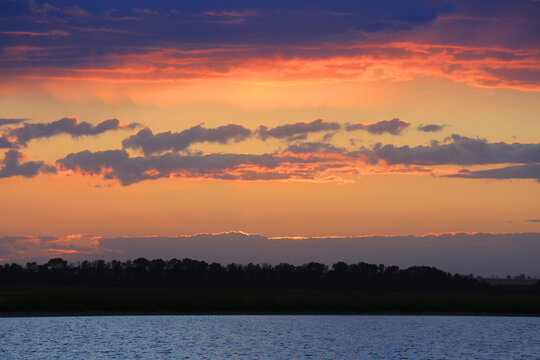 Vibrant sunset paints the sky with fiery orange and deep blue hues over calm water