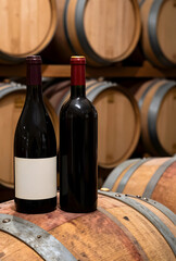 Naklejka premium Wine production and aging process, two red wine bottles on a wooden barrel in a traditional winery cellar