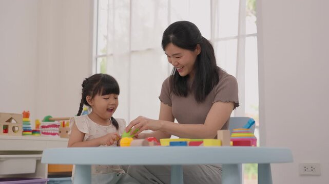 Asian mother and daughter playing with colorful building blocks at home, joyful family learning activity beside bright window, child creativity and connection in warm playroom interior