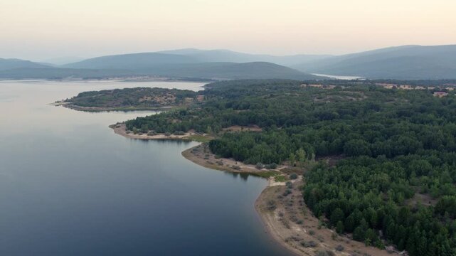 Aerial drone flying over La Cuerda del Pozo Reservoir in Soria with a hazy sky and green forest landscape in Spain