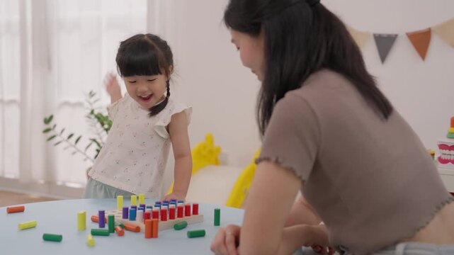 Asian Mother Daughter Child Family Education Game with Colorful Wooden Block Activity at Home, Creative Learning, Joyful Play, Arranging Toys Together Near Bright Window, Engaging Indoor Fun