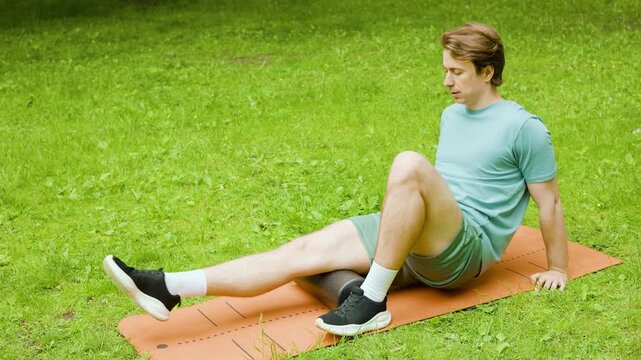 Man outdoors uses a foam roller on his leg for post-workout recovery and myofascial release. This self-massage relieves muscle tension, aiding self-care and rehabilitation. High quality 4k footage