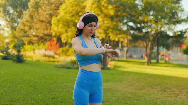 Active young woman checks her smartwatch during outdoor fitness in the sunny park.