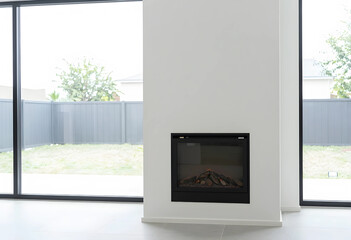 Fototapeta premium Modern home interior with minimalist design, built-in electric fireplace and large glass windows overlooking a backyard