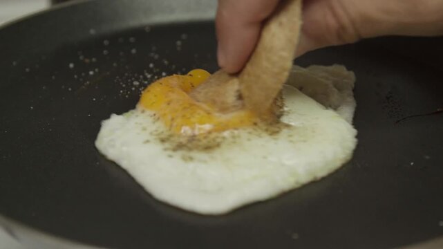 Huevo frito en la sart&eacute;n untando pan en la yema 