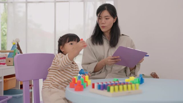 Asian mother and daughter play educational counting game home, helping child develop learning skills, concentration, and confidence while family bonding grows through supportive parent guidance