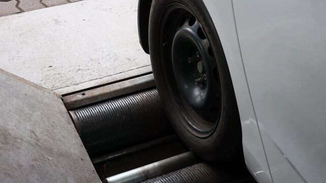 Car wheel runs on roller brake tester during TUV vehicle inspection, measuring braking performance and safety. Workshop equipment checks roadworthiness, maintenance and automotive condition