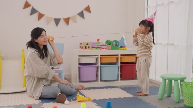 Mother and daughter celebrate colorful indoor birthday party with cake, toys, party decorations, family celebration, playful child activity, and joyful adult moment at home