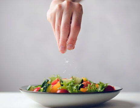 Hand sprinkling salt over a fresh vegetable salad, healthy home cooking, balanced nutrition and meal preparation concept with copy space