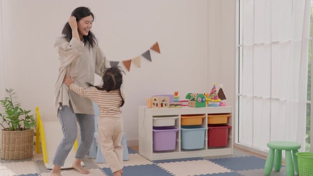 Mother and child dancing in home playroom, joyful family happiness through playful indoor movement, woman sharing affection with child near colorful toy storage and soft natural light at home