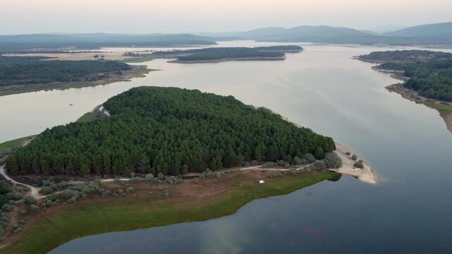 Drone flying over the pine forest peninsula of La Cuerda del Pozo Reservoir in Spain during a tranquil sunset
