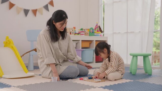Mother and daughter playing wooden building block toy on soft colorful play mat at home, creating warm family moment through calm educational indoor play near sunny window in bright playroom layout