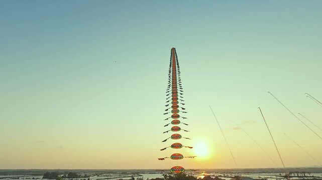 Long Segmented Dragon Kite Climbing Into Sunset Sky Over Village Rooftops