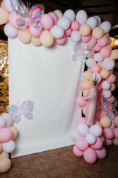 Blank white backdrop framed by pastel balloon arch with butterflies at girl first birthday party