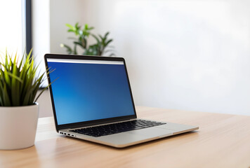 Fototapeta premium Remote work and digital office setup, modern laptop with blank blue screen on a wooden desk with plant, copy space