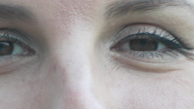 Brown eyes gaze directly at camera as a joyful woman shifts her perspective. Extreme close up shot captures shifting facial focus and fluid movement.